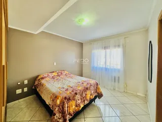 Quarto com cama e janela com cortinas brancas.
