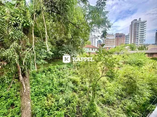 Vista de uma área verde densa com árvores e edifícios residenciais ao fundo.