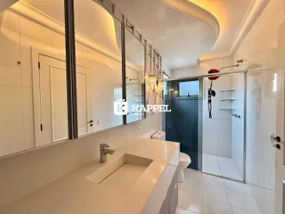 Vista de uma cozinha moderna com bancada branca e área de banheiro com box de vidro.