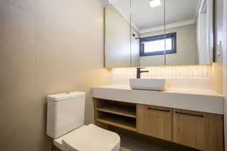 A foto mostra o interior de um banheiro com bancada e armários de madeira.