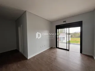 Interior de uma sala com piso de madeira e porta de vidro abrindo para o exterior.