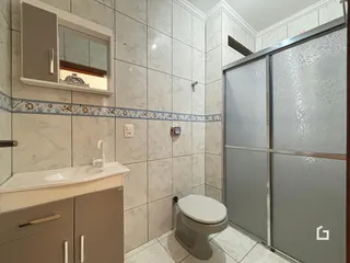 Banheiro com revestimento de azulejos brancos e box de vidro.