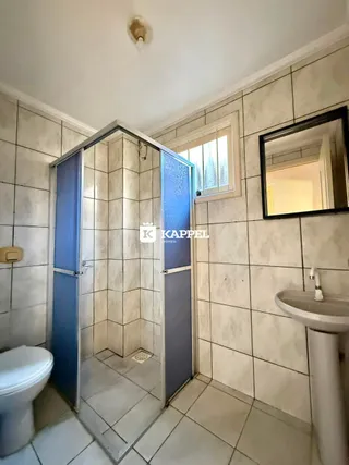 Banheiro com revestimento de azulejos claros e box de vidro.