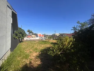 Vista externa de um terreno com grama alta e vegetação ao fundo.