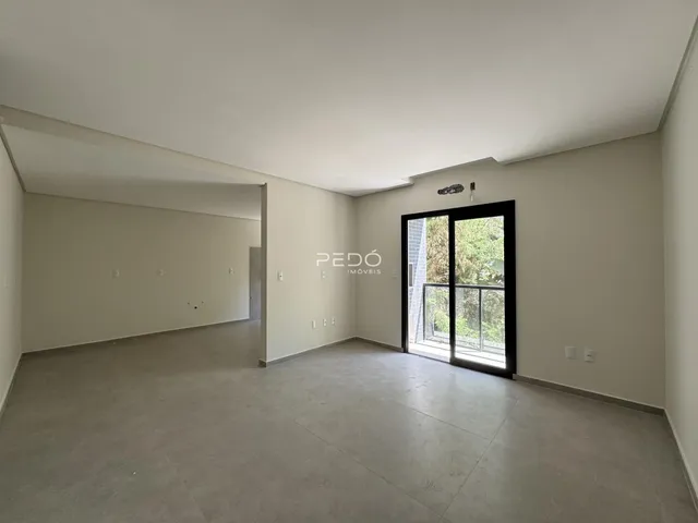 Ambiente interno de uma sala ampla com paredes brancas e piso cinza.