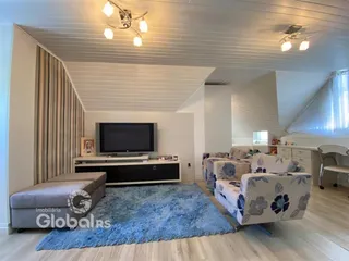 Sala de estar com teto inclinado e grandes janelas em uma residência.