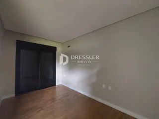 Interior de uma sala com piso de madeira e parede clara.