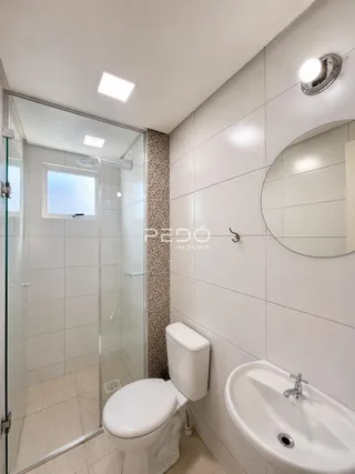 Banheiro com revestimento cerâmico e box de vidro transparente.