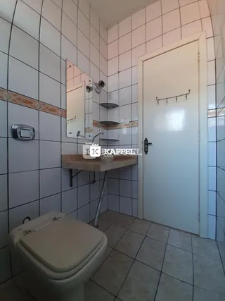 Foto interna de um banheiro com revestimento de azulejos brancos e bancada de madeira.