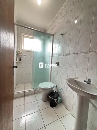 Banheiro com revestimento de azulejos brancos e box de vidro.