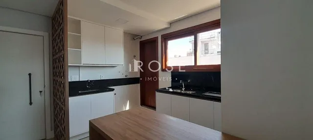 Vista interna de uma cozinha com armários brancos e bancadas escuras.