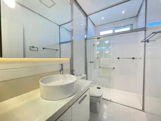 Banheiro moderno com bancada branca e box de vidro transparente.