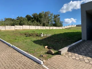 Vista externa de um terreno gramado com cerca de madeira e calçada de tijolos.