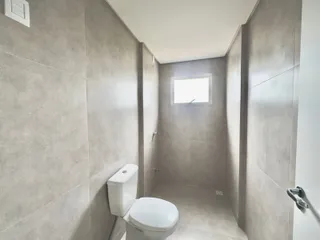 Foto de um banheiro com paredes de azulejo cinza claro e um vaso sanitário branco.