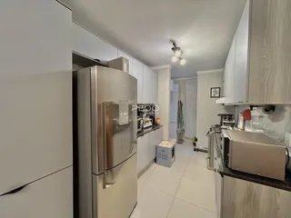 Vista interna de uma cozinha moderna com armários brancos e eletrodomésticos de aço inoxidável.