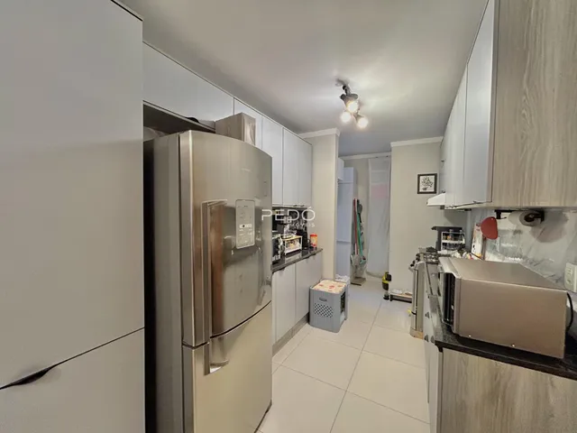 Vista interna de uma cozinha moderna com armários brancos e eletrodomésticos de aço inoxidável.