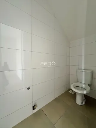 Parede branca com azulejos e um vaso sanitário são visíveis na foto.