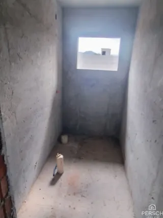Corredor interno com paredes de concreto aparente e piso de cimento.