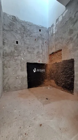 Foto de um interior com paredes de concreto aparente e piso de terra.