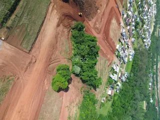 Vista aérea de uma área de terra com vegetação e residências ao fundo.