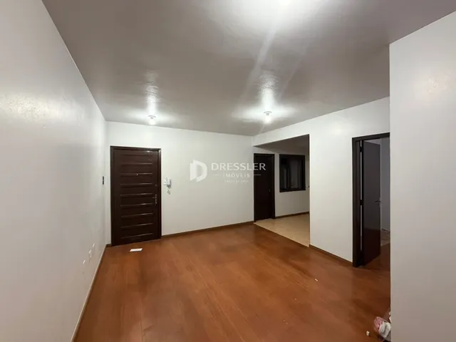 Vista de um corredor interno com piso de madeira e paredes brancas.