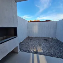 Vista externa com parede branca e piso de cascalho.
