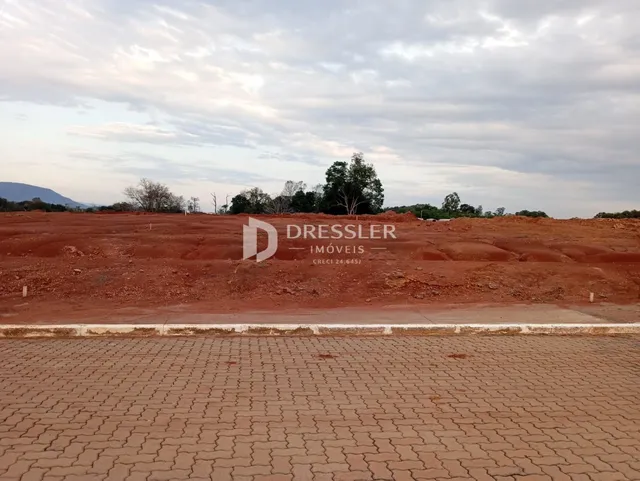 Terreno de terra avermelhada com uma estrada de concreto no primeiro plano.
