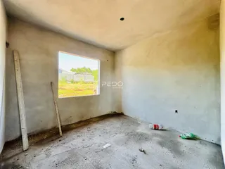 Interior de um cômodo vazio com paredes brancas e piso de concreto cru.