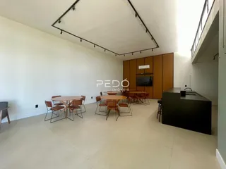 Ambiente interno de uma sala ampla com mesas de jantar e piso claro.