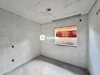 Interior de um cômodo com paredes brancas e piso cru, mostrando a estrutura da construção.