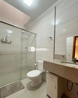 Banheiro com box de vidro e revestimento cerâmico nas paredes.