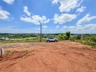 Paisagem de terra vermelha com vegetação ao fundo sob um céu azul.