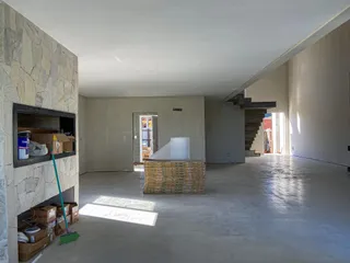 Interior de uma sala ampla em fase de construção com paredes de pedra e piso de concreto.