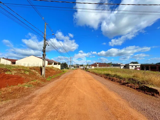 Uma estrada de terra vermelha se estende por uma paisagem rural.