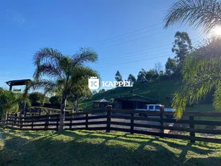 Vista externa de uma propriedade rural com cerca de madeira e vegetação.