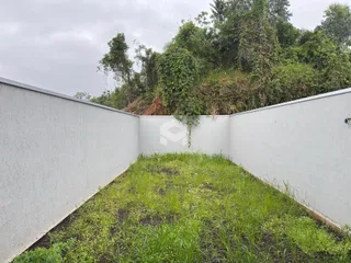 Vista de um pátio cercado por paredes brancas e vegetação densa ao fundo.