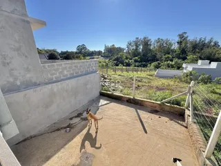 Vista externa de um pátio com cerca e vegetação ao fundo.