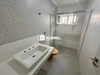 Banheiro moderno com bancada branca e box de vidro transparente.