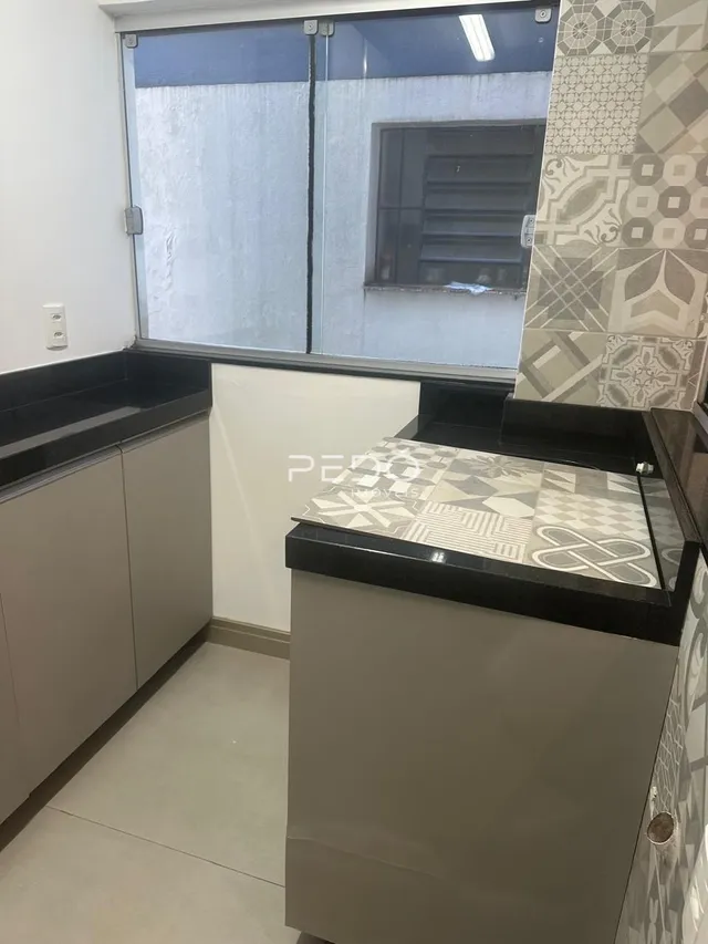 Vista interna de uma cozinha com armários e bancadas escuras.