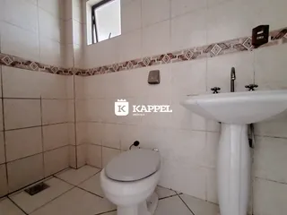 Banheiro com revestimento de azulejos brancos e pia de apoio.