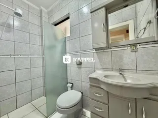 Banheiro com revestimento de azulejos brancos e box de vidro.