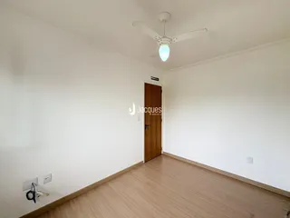 Um corredor interno com paredes brancas e piso de madeira clara.