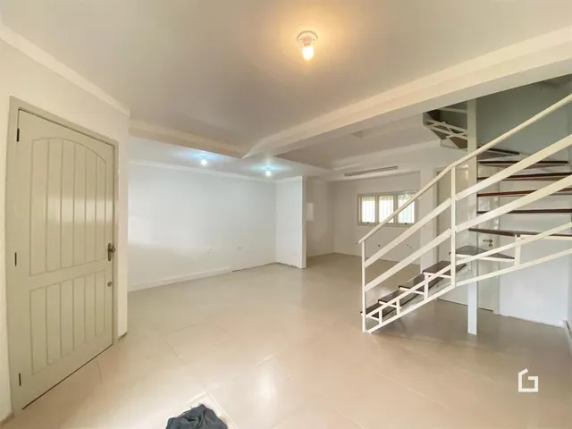 Ambiente interno de uma sala ampla com piso de cerâmica e escadaria em uma residência.