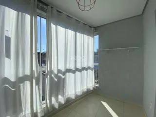 Vista interna de um cômodo com janelas cobertas por cortinas brancas.
