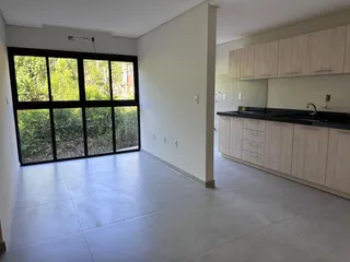 Cozinha com armários brancos e grandes janelas que dão para a vegetação.