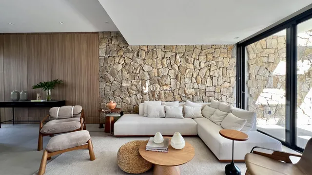 Sala de estar moderna com sofá branco e parede de pedra na residência.