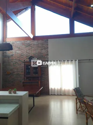 Foto do interior de uma sala com pé direito alto e parede de tijolos aparentes.