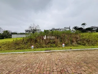 Vista externa de uma propriedade com vegetação alta e piso de tijolos no primeiro plano.
