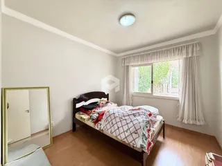 Quarto com cama de madeira e janela com cortinas brancas.