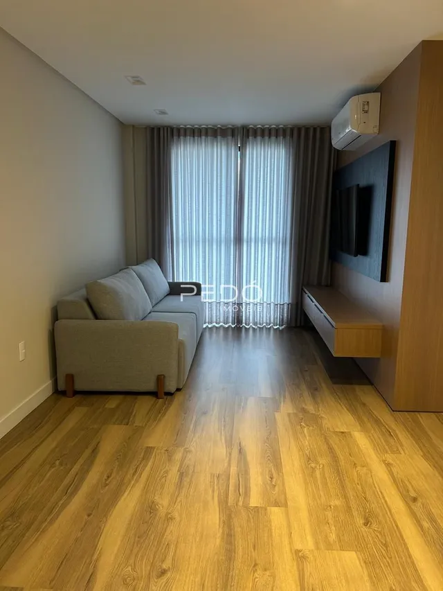 Sala de estar com piso de madeira e cortinas claras.